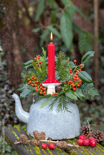 Silvester-Arrangement mit roter Kerze, Stechpalmenzweigen und Koniferenzweigen im alten Teekessel	 photo