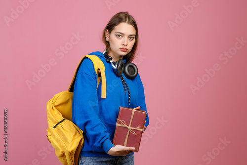 Front view of angry schoolgirl standing, holding bunch of old books. Pretty young student wearing stylish cothes, looking at camera. Concept of education, studying and youth. photo