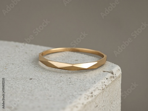 A minimalist geometric gold bangle bracelet with sharp, clean edges, resting on a textured gray concrete slab