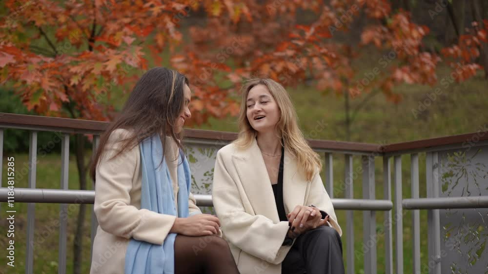 Two joyful women in stylish coats laugh together in a beautiful autumn setting with vibrant foliage Two joyful women in stylish coats laugh together in a beautiful autumn setting with vibrant foliage