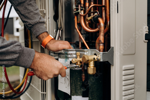 Technician's hands with tools working on the copper pipes of the air conditioner. The photo shows parts of the cooling system and connecting valves.