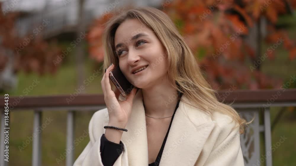A stylish young woman enjoys a wonderful autumn day, happily engaged in a phone conversation amidst colorful leaves A stylish young woman enjoys a wonderful autumn day, happily engaged in a phone conversation amidst colorful leaves