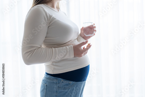 Pregnant woman holding a glass of water, taking vitamins and supplements during pregnancy with copy space. Pregnancy, health, pharmaceuticals. Close up