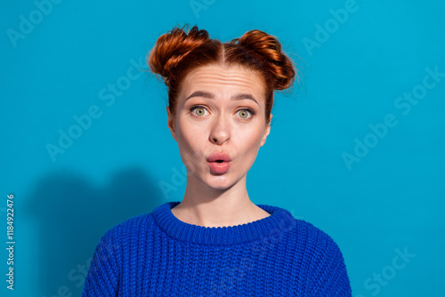 Young woman with expressive face wearing blue sweater standing against vibrant blue background photo