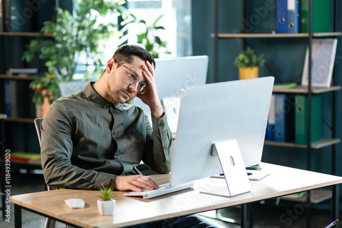Portrait of sad bored business man sitting at desk using pc, leaning head on hand looking at screen. Upset stressed guy suffering job problems, reading bad negative news at office, free copy space
