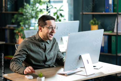 Funny excited surprised man in glasses looking at screen of laptop computer device. Happy lucky guy gets job offer business email, wins a cool prize or earns easy money on gaming website photo