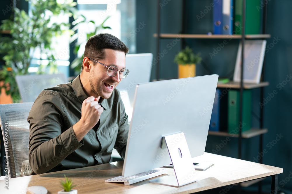 Naklejka premium Excited worker sitting at desk in coworking space use computer reading message looking at device screen received great unbelievable opportunity or reward. Motivated employee celebrating job promotion
