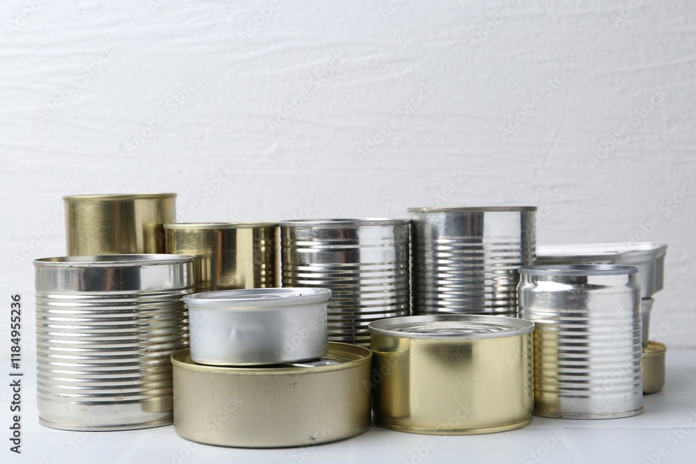 Many closed tin cans on white tiled table, closeup Many closed tin cans on white tiled table, closeup