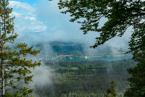 Lush green forest framing panoramic view of Lake Woerth seen from top of Kathreinkogel in Schiefling am See, Carinthia, Austria. Rolling hills in idyllic serene landscape in Austrian Alps in spring photo