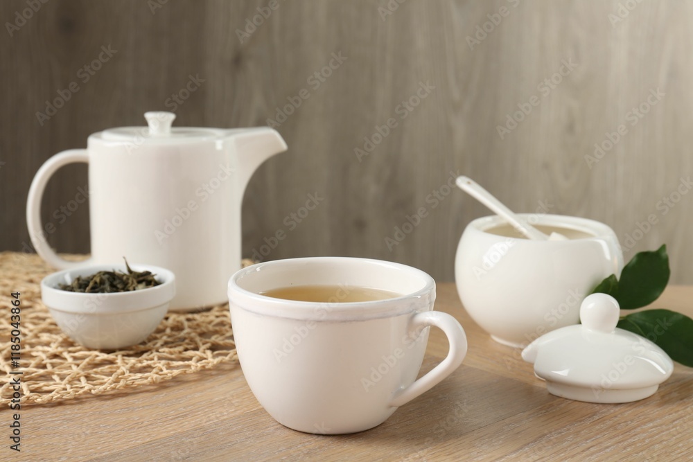 Refreshing green tea in cup, sugar bowl, leaves and teapot on wooden table Refreshing green tea in cup, sugar bowl, leaves and teapot on wooden table