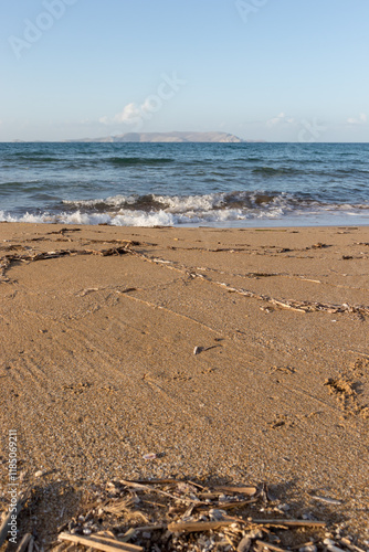 Sandy beach with waves. Close-up view of sand with sea waves and an island in the background