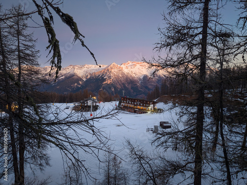 Early pink morning aerial of ski resort Vialattea in Italian Alps with mountain hut and lifts seen through pine tree forest photo