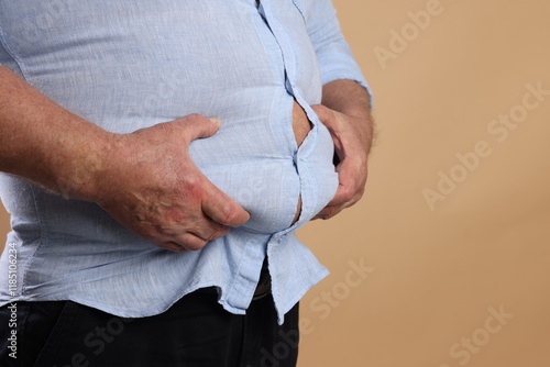 Overweight man in tight shirt on beige background, closeup. Space for text photo