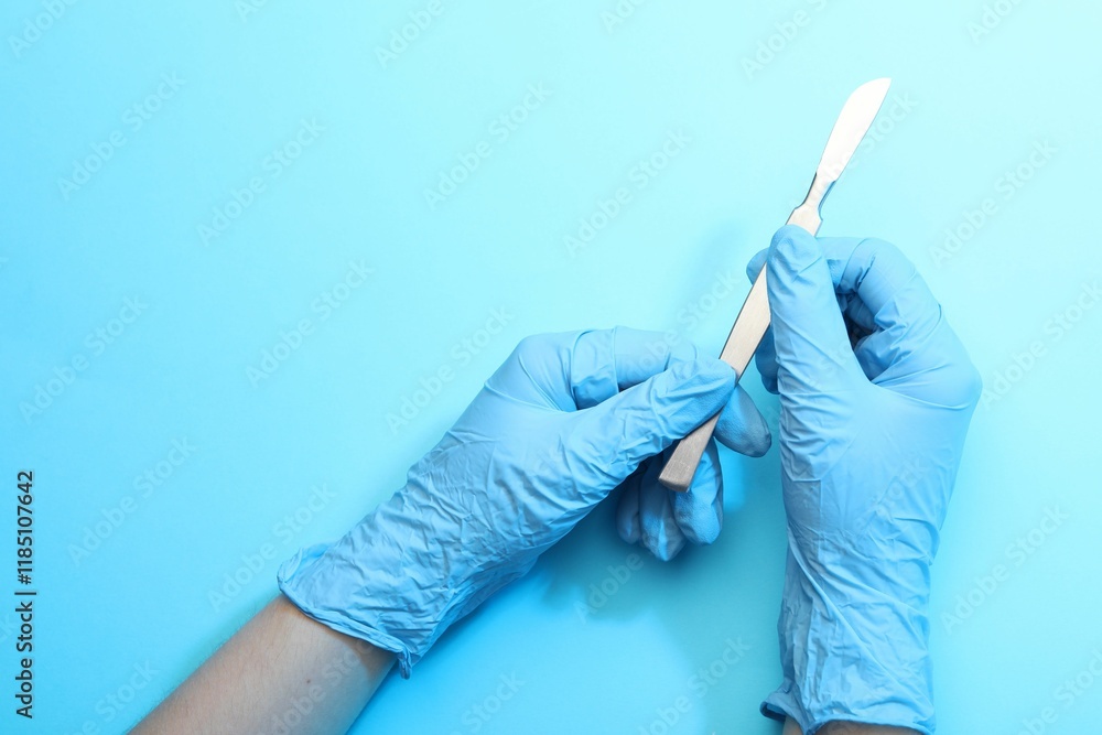 Fototapeta premium Doctor with surgical scalpel on light blue background, top view. Space for text