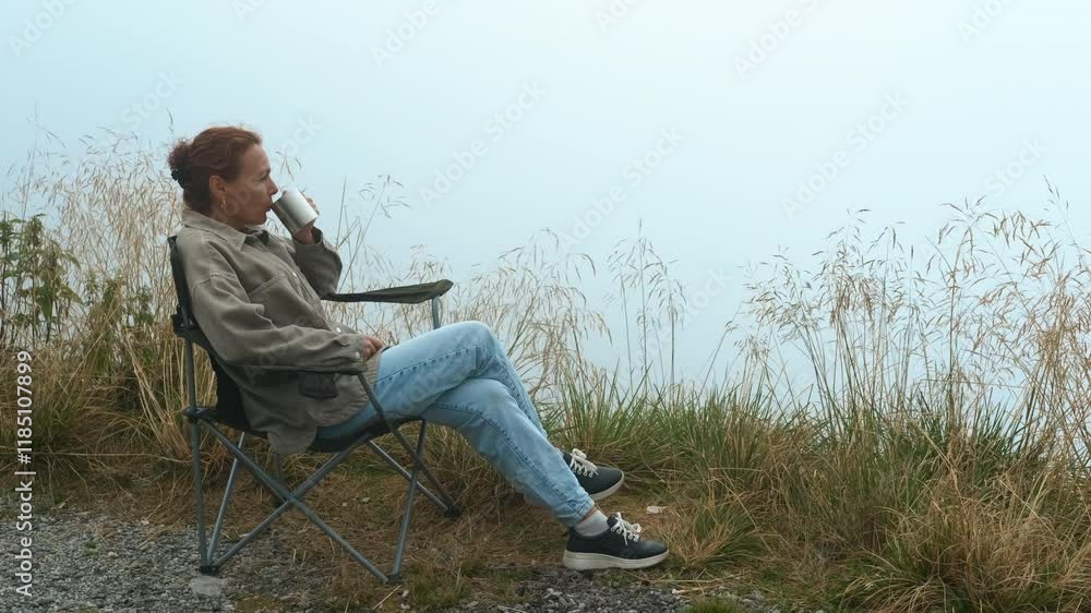 Coffee in the mountains. Woman sits in a folding chair, sipping from her mug and savoring the fresh air while surrounded by the beauty of nature. Peaceful moments unfold in a serene outdoor setting Coffee in the mountains. Woman sits in a folding chair, sipping from her mug and savoring the fresh air while surrounded by the beauty of nature. Peaceful moments unfold in a serene outdoor setting