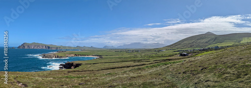 Panoramic view under blue cloudy sky over the green meadows of west Ireland in County Kerry overlooking Clogher beach