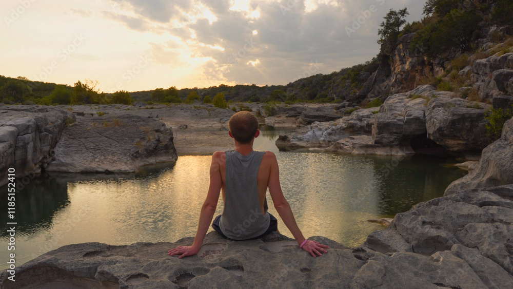 Man sitting along river during sunset at Pedernales Falls State Park near Austin, Texas USA Man sitting along river during sunset at Pedernales Falls State Park near Austin, Texas USA