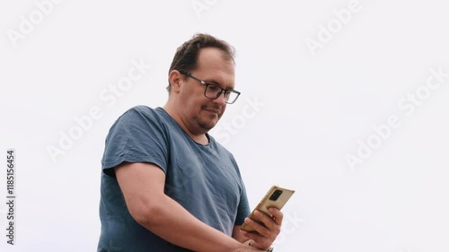 Adult caucasian man, unshaven in glasses and blue t-shirt attentively reads a message on smartphone or types text with serious face. Millennial plus size guy portrait. People and emotions concept.