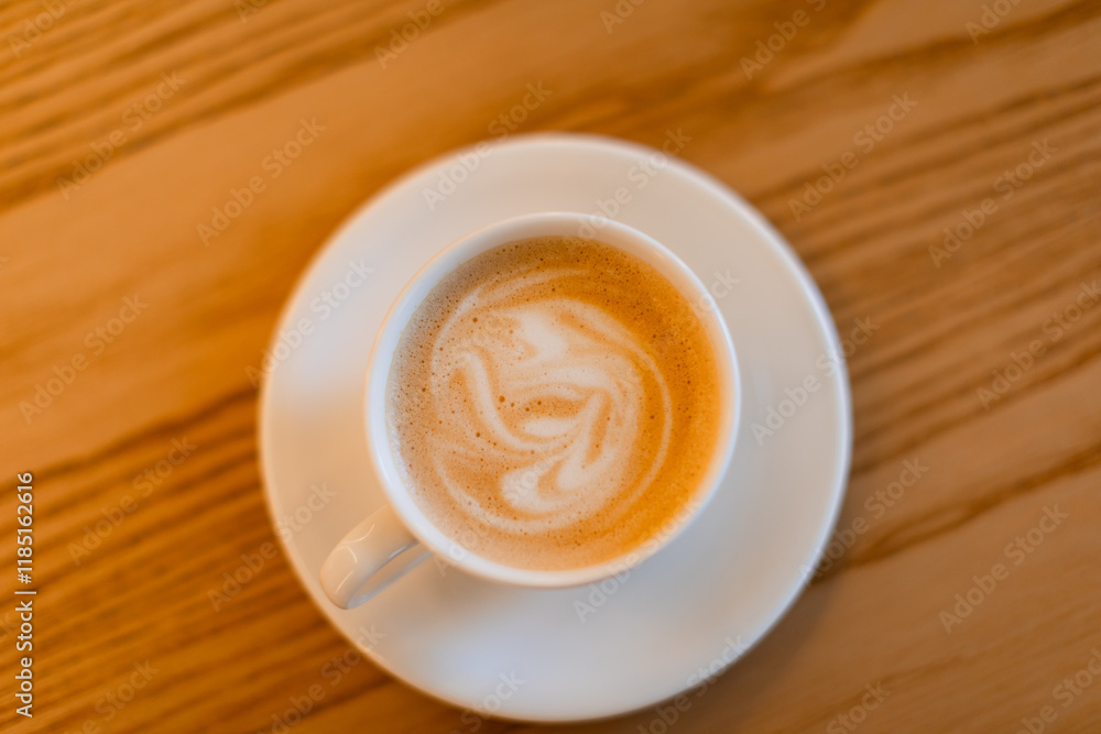 A classic cappuccino with delicate latte art served in a white ceramic cup on a matching saucer with a silver spoon. The warm wooden table adds a cozy coffee shop ambiance. A classic cappuccino with delicate latte art served in a white ceramic cup on a matching saucer with a silver spoon. The warm wooden table adds a cozy coffee shop ambiance.