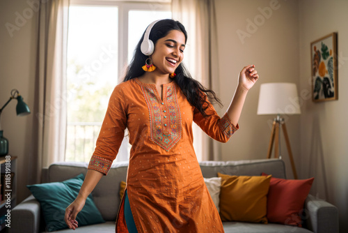 Happy young Indian woman wearing traditional clothes listening to music with headphones at home and dancing
