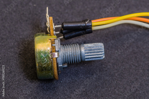 A metal potentiometer with wires attached, lying on a dark background photo