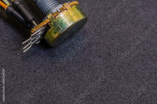 A metallic potentiometer connected with wires on a dark surface photo