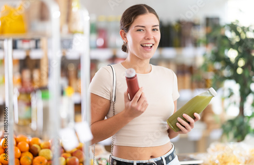 Girl hold bottle, choose and buy smoothie in store. Market visitor consider make choice blended fruit cocktail. Client hesitates before buying, choose smoothie, reads labels on bottles photo