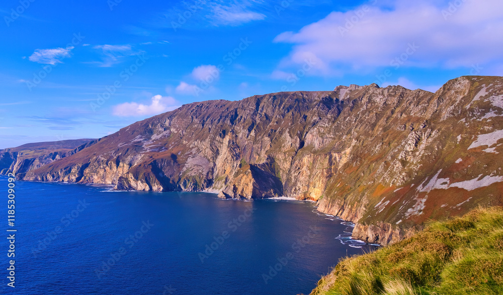 Slieve League in Donegal Ireland - the highest cliffs in Europe - Experience a breathtaking view of rugged cliffs merging with the calm ocean under a partly cloudy sky Slieve League in Donegal Ireland - the highest cliffs in Europe - Experience a breathtaking view of rugged cliffs merging with the calm ocean under a partly cloudy sky
