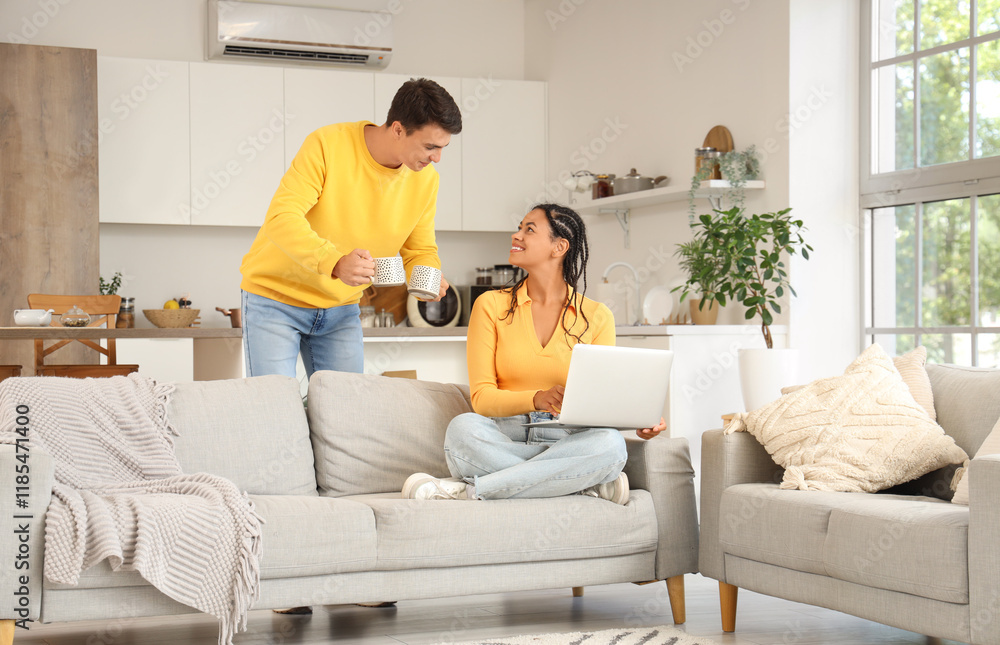 Young couple with cups of coffee using laptop in kitchen Young couple with cups of coffee using laptop in kitchen