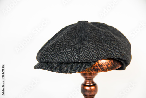 Detail of a black herringbone newsboy hat mounted on a bronze mannequin head on a white background. concept photo of a classic newsboy hat in jet black on a bronze mannequin