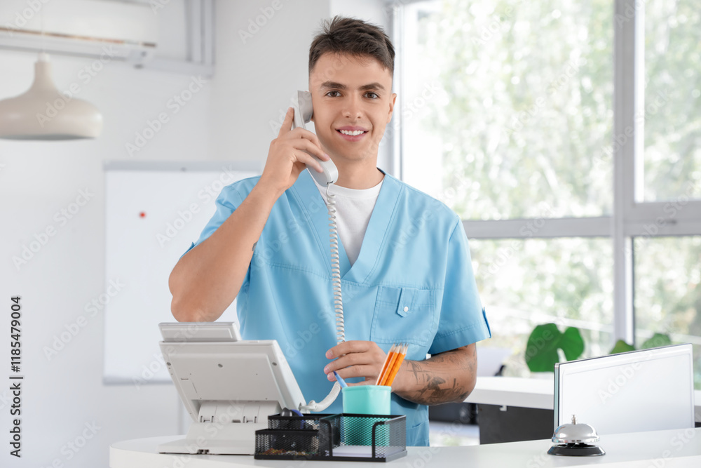 © Pixel-Shot - Male medical intern talking by telephone at reception in clinic