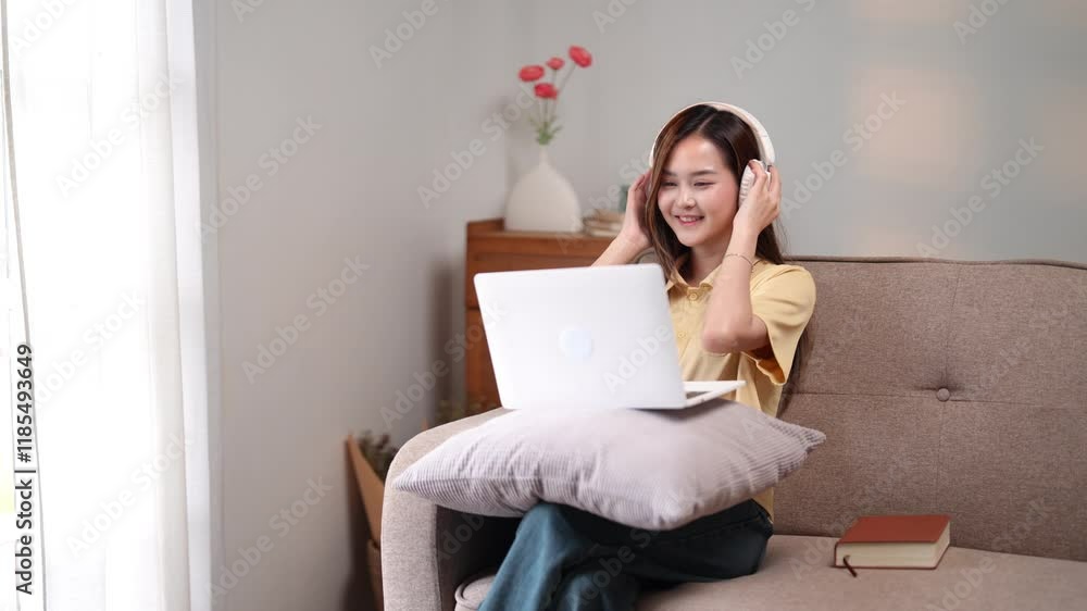 A woman wearing headphones while using a laptop on a couch, enjoying a productive moment at home A woman wearing headphones while using a laptop on a couch, enjoying a productive moment at home