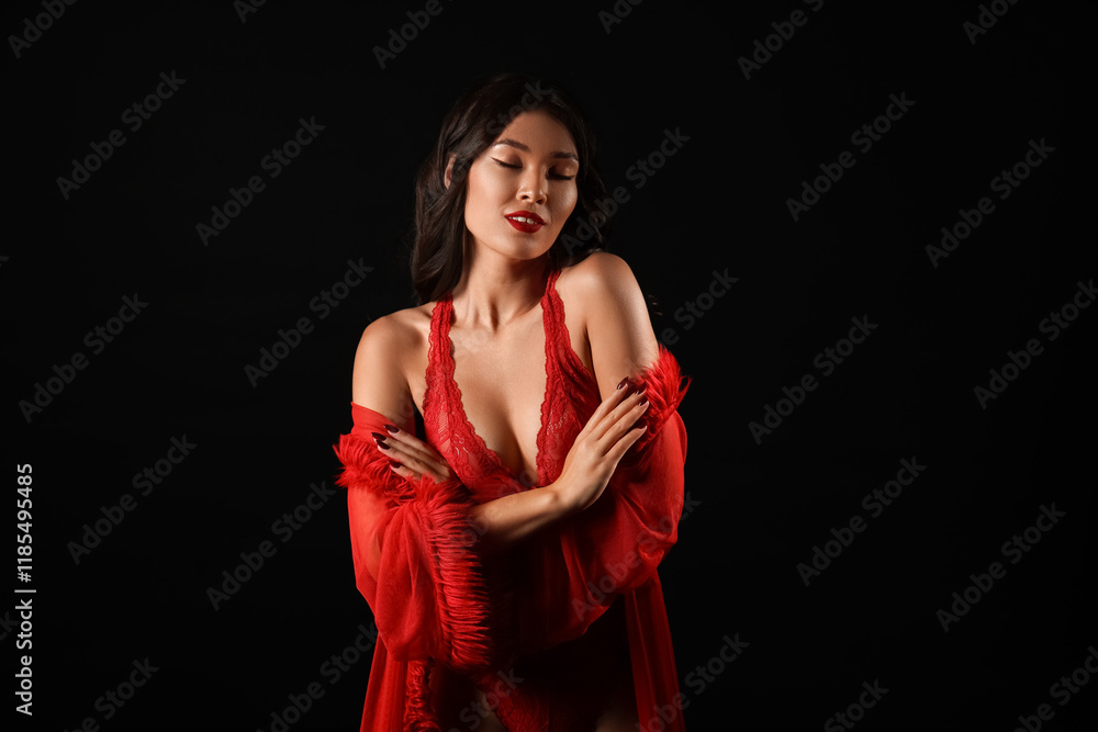Fototapeta premium Beautiful young Asian woman in sexy underwear and red peignoir on black background