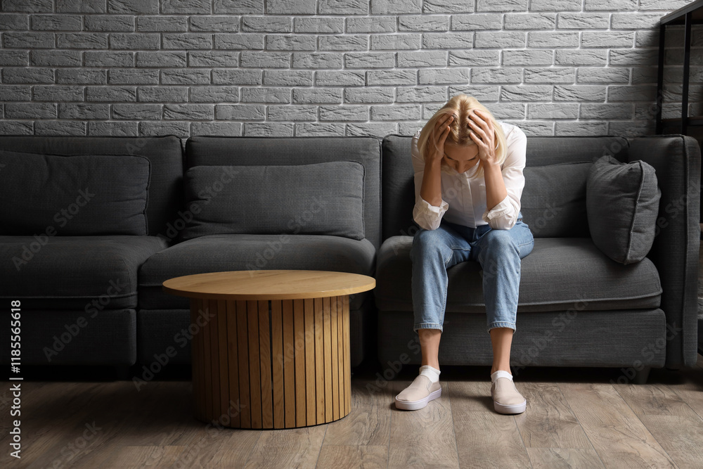 Fotografie Worried mature woman sitting on sofa at home