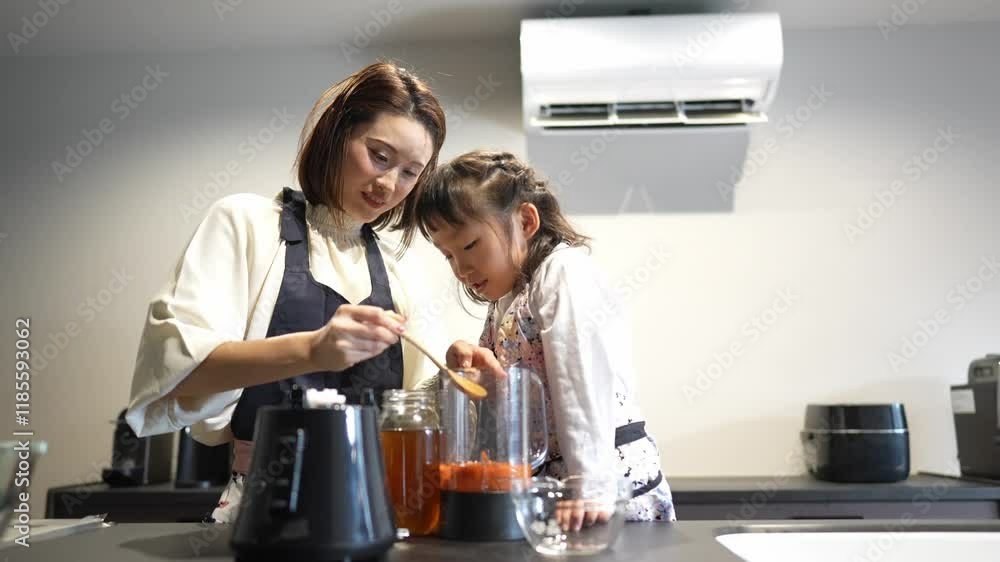 A Japanese parent and child, a woman in her 30s and a 6-year-old girl, are wearing aprons and making juice by putting carrots and honey in a blender in their home kitchen. Slow motion video. A Japanese parent and child, a woman in her 30s and a 6-year-old girl, are wearing aprons and making juice by putting carrots and honey in a blender in their home kitchen. Slow motion video.