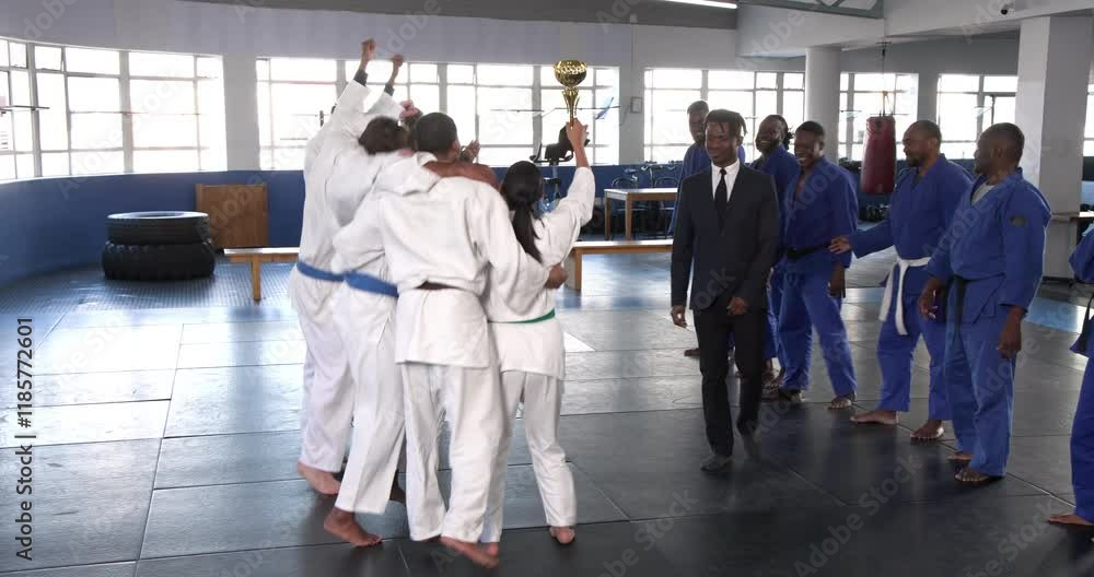 Celebrating victory, judo team in white uniforms holding trophy in dojo Celebrating victory, judo team in white uniforms holding trophy in dojo