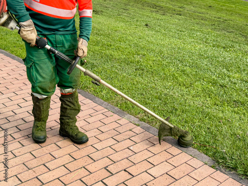 Gardener using trimmer to maintain lawn edge near brick pathway
