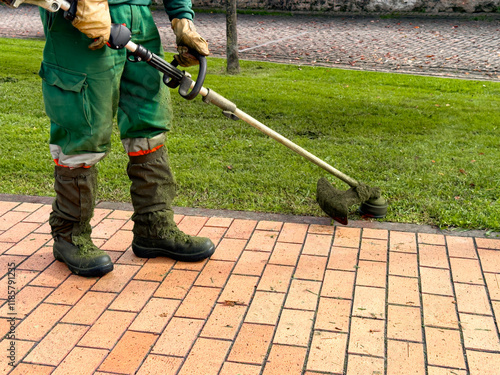 Caucasian male adult using lawn trimmer on brick pathway in park photo