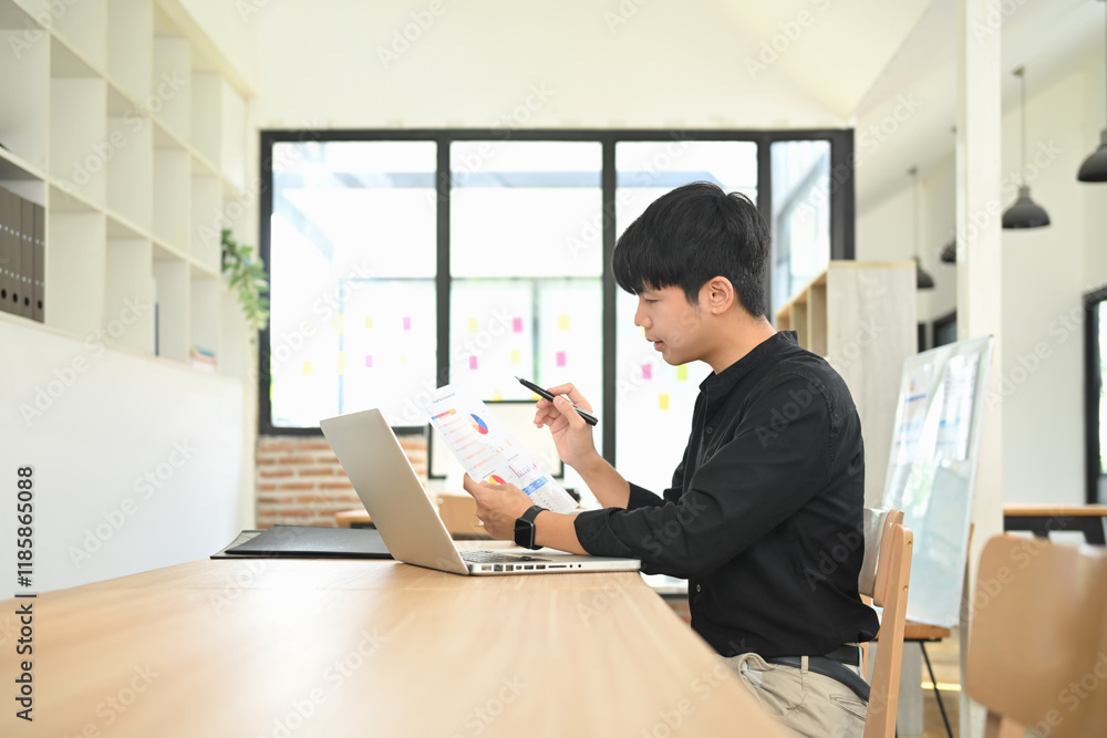 Young businessman reviewing report with charts and graphs while working on a laptop. Young businessman reviewing report with charts and graphs while working on a laptop.