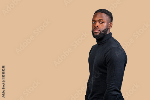 Serious young man wearing black turtleneck posing on beige background