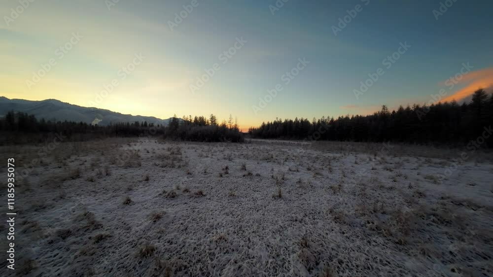 A tranquil meadow lies blanketed in frost as the sun rises slowly over the mountains. The peaceful scene showcases the beauty of winter’s early light and nature’s stillness. A tranquil meadow lies blanketed in frost as the sun rises slowly over the mountains. The peaceful scene showcases the beauty of winter’s early light and nature’s stillness.