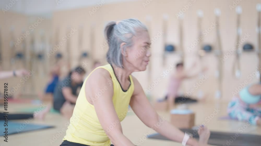 A woman is practicing yoga poses in a room with other people. The atmosphere is serene and tranquil, as everyone focuses on their movements and breathing. The woman is in the middle of a pose A woman is practicing yoga poses in a room with other people. The atmosphere is serene and tranquil, as everyone focuses on their movements and breathing. The woman is in the middle of a pose