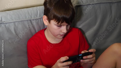 ten year old boy playing smartphone sitting on sofa