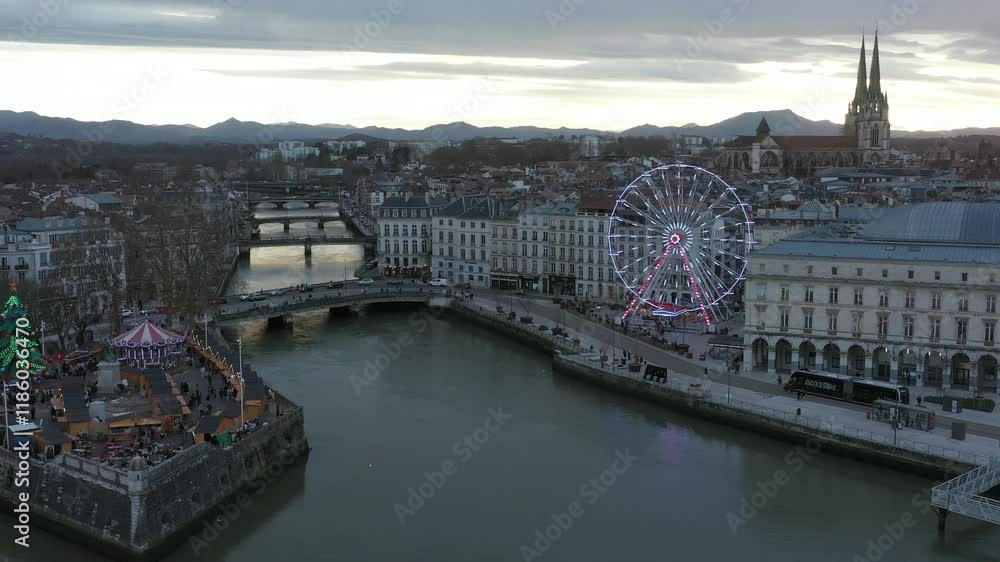 Christmas in Bayonne along Adour River at sunset, Ferris wheel, Cathedral in background, cityscape, France. Aerial drone view