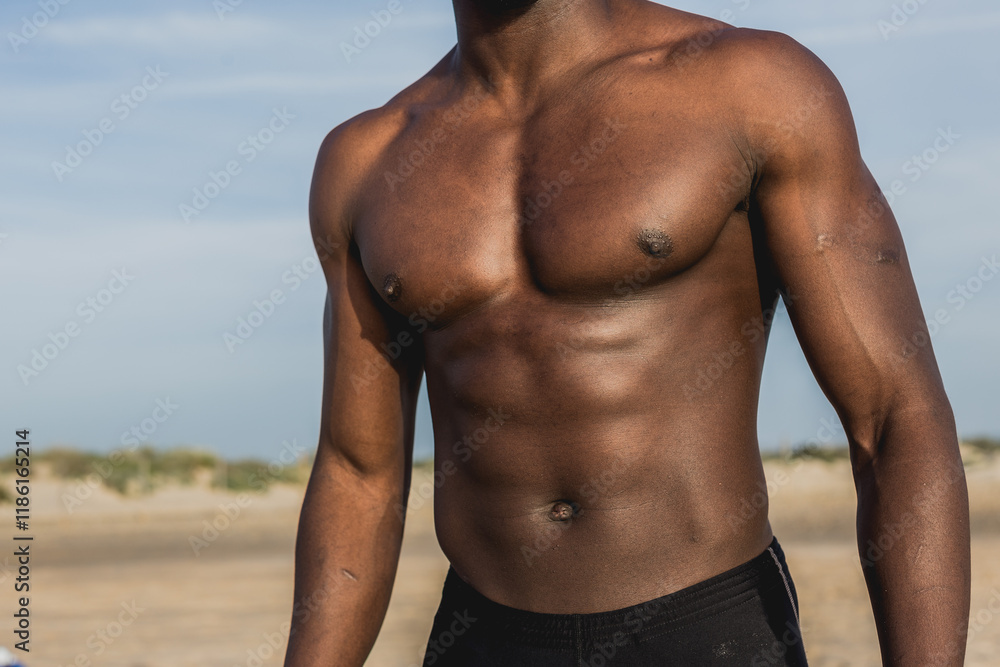 Fototapeta premium Muscular young black man posing on the beach with no shirt, showcasing abs