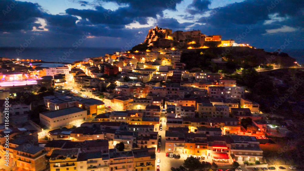 Fototapeta premium Stunning nighttime drone shot of Castelsardo with glowing lights and coastal charm in Sardinia