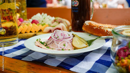 Fototapeta Naklejka Na Ścianę i Meble -  Bayerischer Wurstsalat mit Breze und Spezi im Biergarten auf blau-weißer Tischdecke serviert