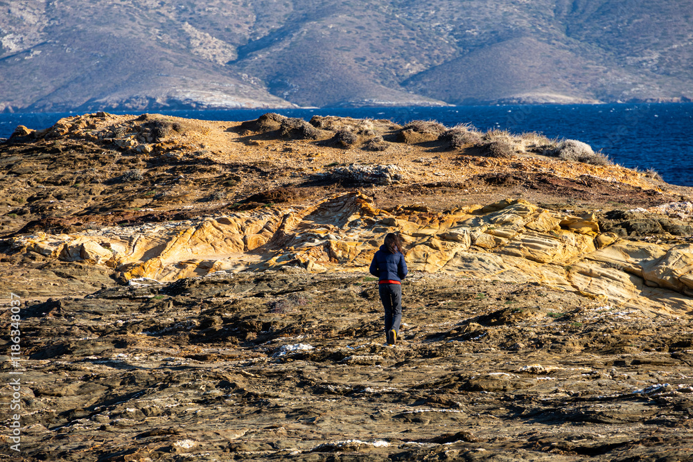 Woman standing alone on the cliffs from an island in the middle of the sea. Concept image for solitude and loneliness. Woman photographed from behind.