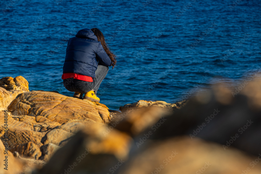 Woman standing alone on the cliffs from an island in the middle of the sea. Concept image for solitude and loneliness. Woman photographed from behind.