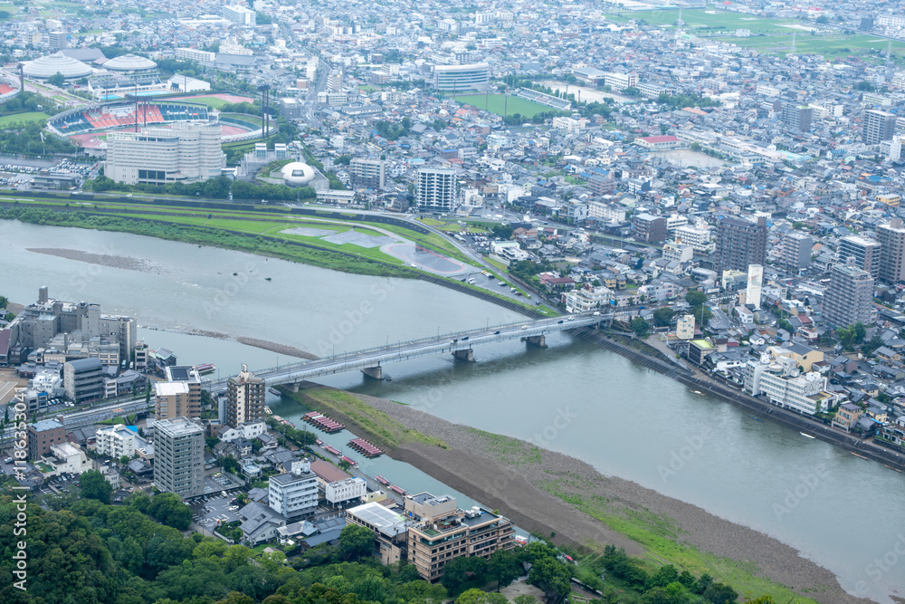 Fototapeta premium A bird's-eye view of a regional Japanese city, Gifu, Japan, shows a sprawling urban landscape with a dense network of roads and buildings along the Nagara River, with a bridge connecting the city. 岐阜市